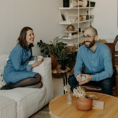 un couple rit dans un salon avec une tasse à la main